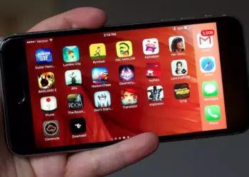 Tampilan homescreen iPhone yang dipegang tangan, dipenuhi berbagai ikon Game iPhone Gratis populer dan aplikasi media sosial.