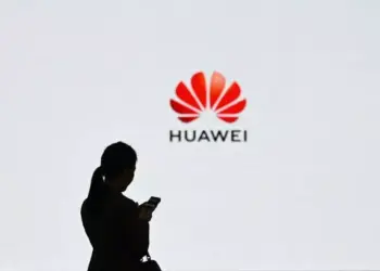 Siluet seorang wanita memegang ponsel di depan layar besar dengan logo merah Huawei, melambangkan popularitas perangkat ini di kalangan pengguna muda seperti pelajar.