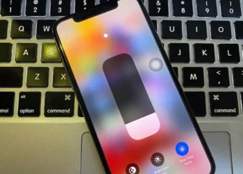Layar iPhone menampilkan Control Center dengan slider kecerahan, menunjukkan opsi untuk True Tone aktif (Nyala) dan Night Shift.
