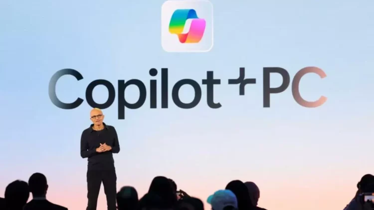 Satya Nadella mengumumkan Copilot+ PC di atas panggung dengan logo "Copilot+PC" besar.