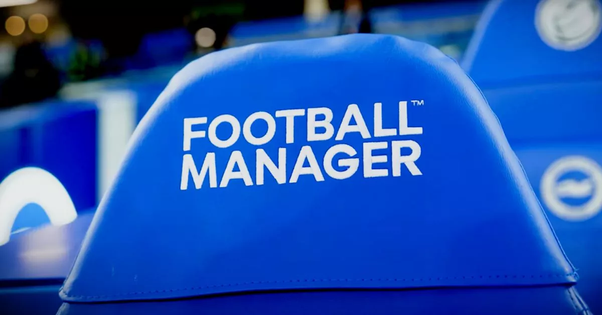 Close-up kursi pelatih berwarna biru dengan tulisan "FOOTBALL MANAGER" di stadion.