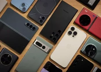 Berbagai macam ponsel flagship (Samsung, iPhone, Google Pixel, Vivo, dll.) bertebaran di atas meja kayu.