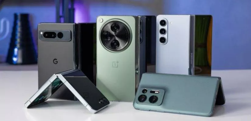 Beberapa ponsel flagship (Pixel, OnePlus, Samsung Fold) disusun berdiri dan terlipat di atas meja.