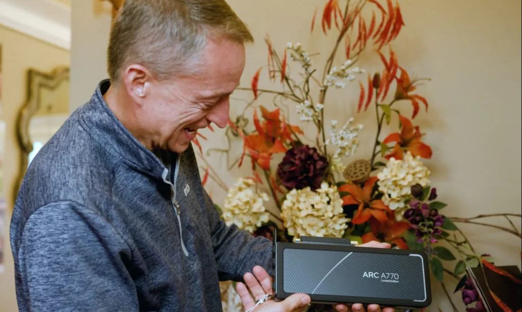 CEO Intel, Pat Gelsinger, tersenyum sambil memegang kartu grafis Intel Arc A770, menunjukkan komitmen perusahaan terhadap masa depan dan nasib Intel Arc.