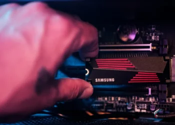 Tangan sedang memasang SSD Samsung M.2 NVMe ke motherboard PC, mengilustrasikan proses upgrade atau perakitan PC yang terancam kenaikan harga komponen SSD.