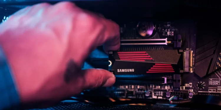 Tangan sedang memasang SSD Samsung M.2 NVMe ke motherboard PC, mengilustrasikan proses upgrade atau perakitan PC yang terancam kenaikan harga komponen SSD.
