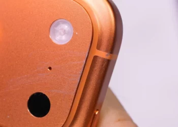 Close-up goresan mikro pada bodi iPhone 17 Pro berwarna oranye, mengilustrasikan kelemahan iPhone 17 Pro yang rentan terkelupas di bagian ujung kamera.