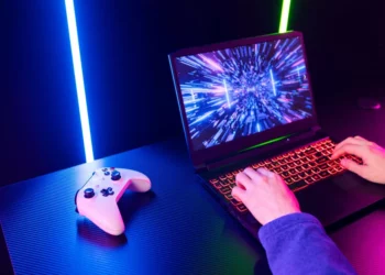 Seorang gamer sedang memilih laptop gaming terbaik 2025 di meja dengan setup lampu RGB dan controller.