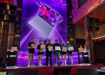 Lima orang eksekutif Axioo dan AMD memegang produk laptop di panggung peluncuran Axioo Hype R X8 OLEO, dengan layar LED besar menampilkan laptop.