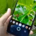 Tangan memegang smartphone Infinix yang digunakan untuk memotret daun hijau, menampilkan antarmuka kamera dengan berbagai mode dan kontrol.