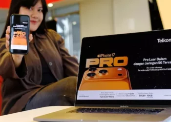 Wanita menunjukkan iPhone 17 Pro dan promosi pre-order Telkomsel di laptop