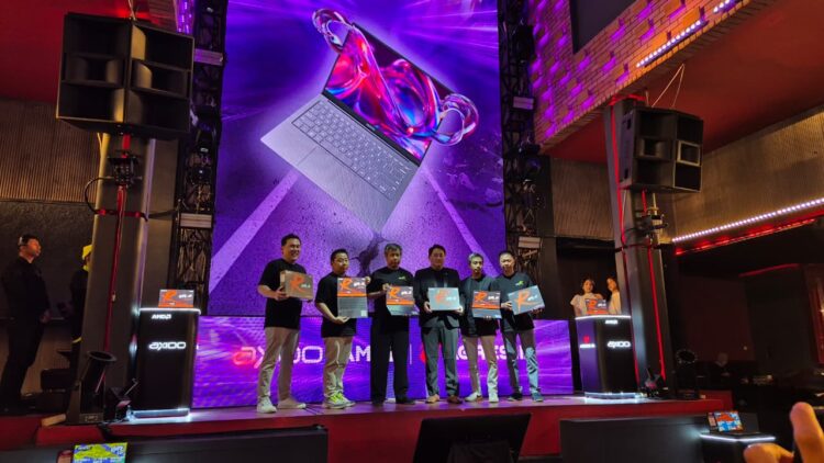 Lima orang eksekutif Axioo dan AMD memegang produk laptop di panggung peluncuran Axioo Hype R X8 OLEO, dengan layar LED besar menampilkan laptop.