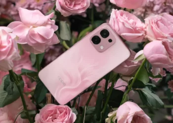 Ponsel OPPO A6 Pro berwarna pink dengan pola unik di bagian belakang, diletakkan di antara bunga mawar merah muda yang mekar