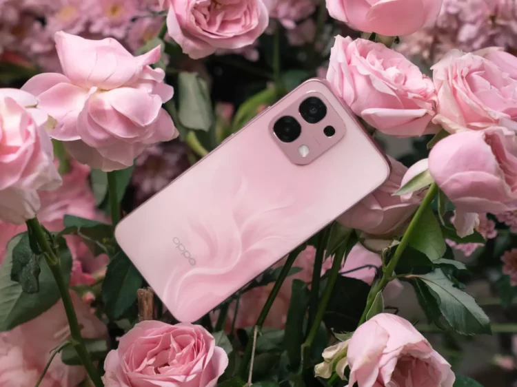 Ponsel OPPO A6 Pro berwarna pink dengan pola unik di bagian belakang, diletakkan di antara bunga mawar merah muda yang mekar