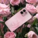 Ponsel OPPO A6 Pro berwarna pink dengan pola unik di bagian belakang, diletakkan di antara bunga mawar merah muda yang mekar