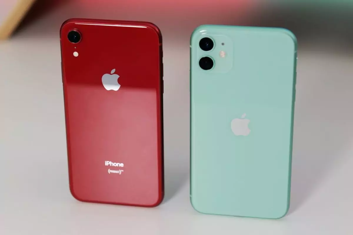 Dua iPhone, satu merah (iPhone XR) dan satu hijau mint (iPhone 11), diletakkan berdampingan, menyoroti perbedaan desain kamera belakang.