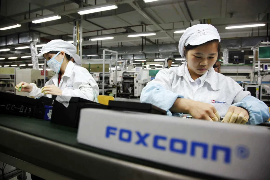 Pekerja di pabrik Foxconn sedang merakit komponen di jalur perakitan, sebagai ilustrasi peran Foxconn dalam produksi engsel iPhone Lipat.