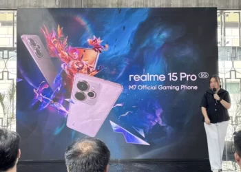 Seorang presenter wanita berdiri di depan layar besar yang menampilkan dua unit ponsel realme 15 Pro 5G, logo M7 World Championship, dan teks 'realme 15 Pro 5G M7 Official Gaming Phone