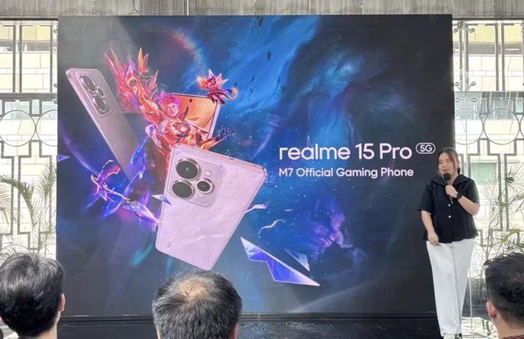 Seorang presenter wanita berdiri di depan layar besar yang menampilkan dua unit ponsel realme 15 Pro 5G, logo M7 World Championship, dan teks 'realme 15 Pro 5G M7 Official Gaming Phone