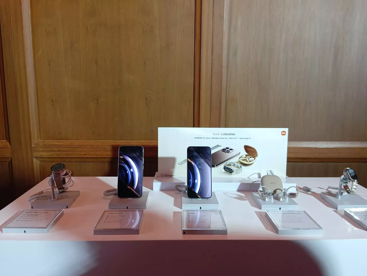 Berbagai perangkat "Gold Collection" Xiaomi seperti smartphone, smartwatch, dan earbud, dipamerkan di atas meja display dalam sebuah acara.