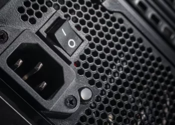 Seorang teknisi atau builder PC sedang memasang komponen PSU ke dalam casing PC gaming berwarna putih.