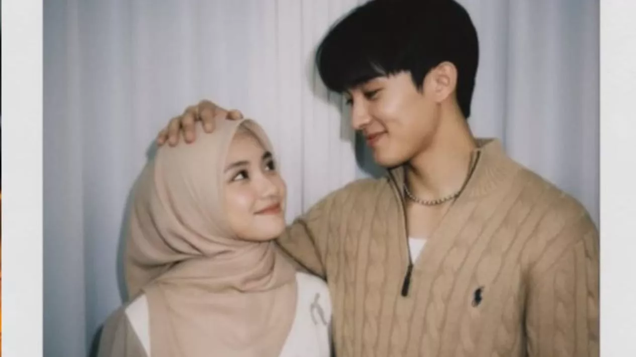 Foto polaroid realistis seorang pria muda tersenyum memegang kepala wanita berhijab yang juga tersenyum menatapnya.