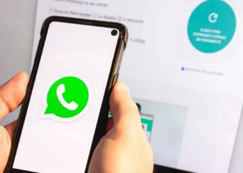 Logo aplikasi WhatsApp berwarna hijau ditampilkan di layar smartphone Android yang sedang dipegang.