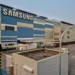 Gedung pabrik dan fasilitas besar Samsung dengan logo raksasa berwarna biru, melambangkan basis produksi global.