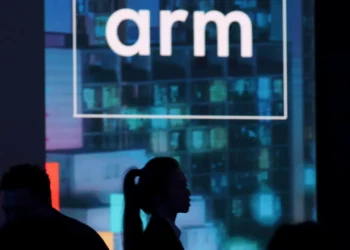 Logo perusahaan ARM ditampilkan di layar besar pada sebuah acara, menggambarkan peran penting prosesor ARM sebagai kekuatan tersembunyi di industri teknologi.