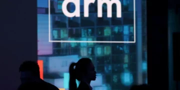 Logo perusahaan ARM ditampilkan di layar besar pada sebuah acara, menggambarkan peran penting prosesor ARM sebagai kekuatan tersembunyi di industri teknologi.