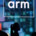Logo perusahaan ARM ditampilkan di layar besar pada sebuah acara, menggambarkan peran penting prosesor ARM sebagai kekuatan tersembunyi di industri teknologi.