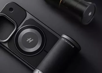 Aksesori kamera smartphone hitam dengan Teknologi Hasselblad dan cincin magnetik, diletakkan di samping lensa kamera eksternal, di latar belakang gelap.