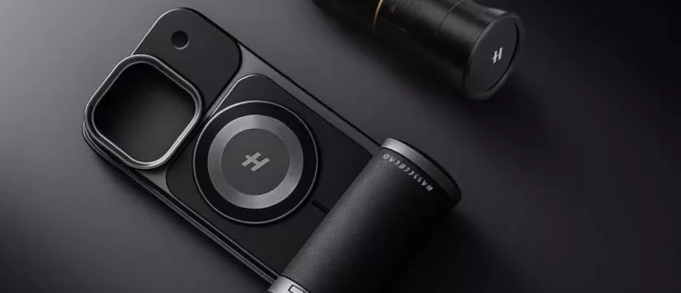 Aksesori kamera smartphone hitam dengan Teknologi Hasselblad dan cincin magnetik, diletakkan di samping lensa kamera eksternal, di latar belakang gelap.