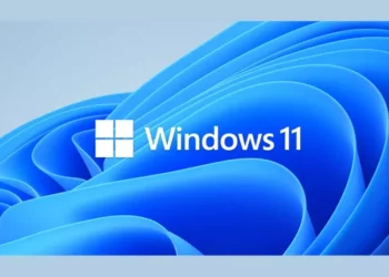 Logo Windows 11 berwarna putih di atas latar belakang wallpaper biru bergelombang yang khas, merepresentasikan sistem operasi terbaru Microsoft.