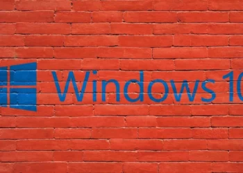 Logo dan tulisan "Windows 10" berwarna biru yang dicat di atas dinding bata merah, melambangkan sistem operasi yang sudah usang.