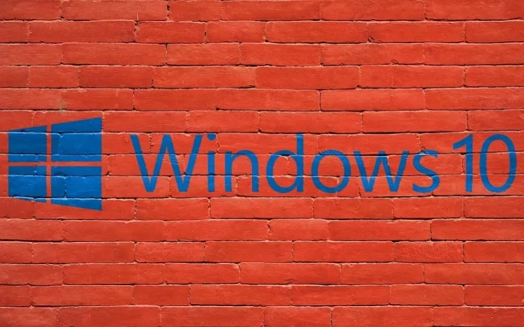 Logo dan tulisan "Windows 10" berwarna biru yang dicat di atas dinding bata merah, melambangkan sistem operasi yang sudah usang.