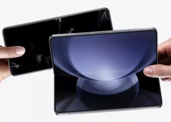 Dua tangan saling bertukar, satu memegang smartphone dengan layar retak dan satu lagi memegang smartphone lipat baru yang mulus, melambangkan program trade-in.