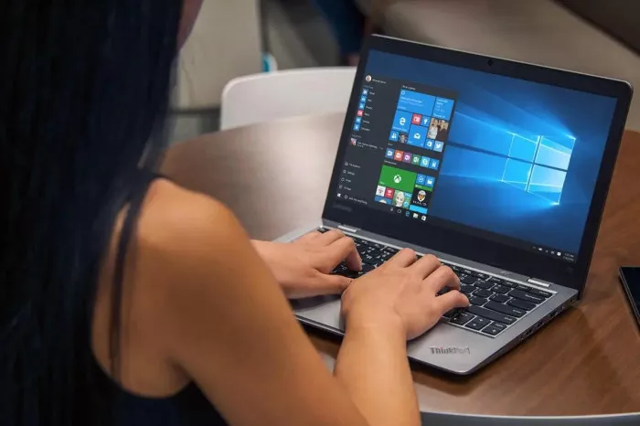 Seorang wanita menggunakan laptop dengan antarmuka awal Windows 10, menunjukkan aktivitas komputasi harian.