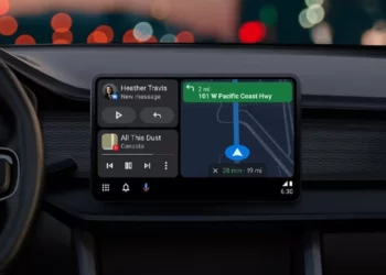 Tampilan layar dashboard mobil yang menjalankan antarmuka Android Auto, menampilkan navigasi peta, notifikasi pesan, dan kontrol musik.