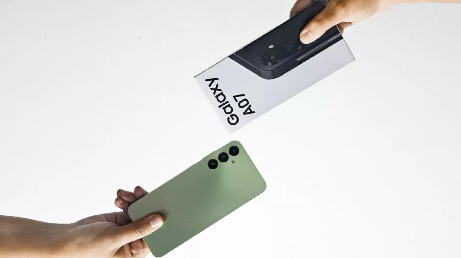 Dua tangan saling bertukar, satu menyerahkan kotak smartphone "Galaxy A07" dan satu lagi menerima smartphone Samsung berwarna hijau.