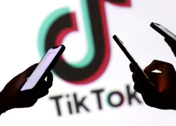 Beberapa tangan memegang smartphone dengan logo TikTok di latar belakang, mengilustrasikan ketidakpastian nasib TikTok Shop.