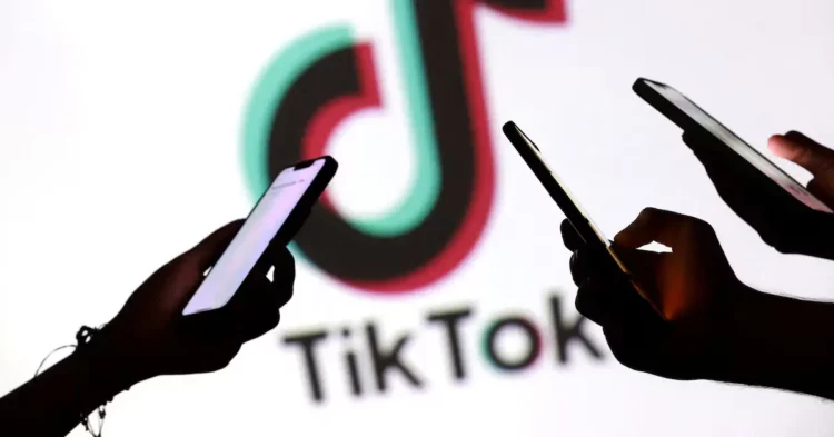 Beberapa tangan memegang smartphone dengan logo TikTok di latar belakang, mengilustrasikan ketidakpastian nasib TikTok Shop.
