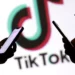 Beberapa tangan memegang smartphone dengan logo TikTok di latar belakang, mengilustrasikan ketidakpastian nasib TikTok Shop.