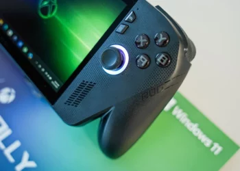 Sebuah foto close-up dari handheld gaming PC ROG Xbox Ally berwarna hitam, menyorot detail joystick kanan yang menyala dan tombol ABXY yang ikonik di atas materi promosi Windows 11.