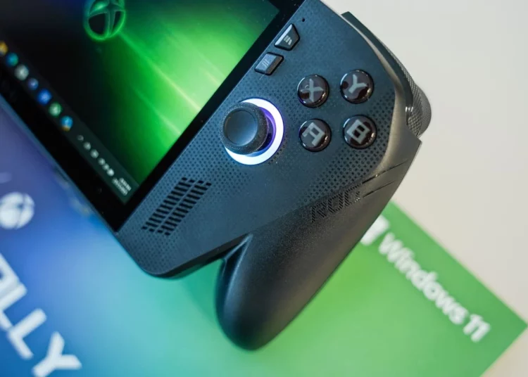 Sebuah foto close-up dari handheld gaming PC ROG Xbox Ally berwarna hitam, menyorot detail joystick kanan yang menyala dan tombol ABXY yang ikonik di atas materi promosi Windows 11.