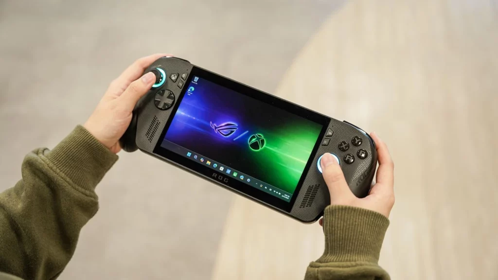Sepasang tangan sedang memegang handheld gaming PC ROG Xbox Ally berwarna hitam, menampilkan antarmuka Xbox Fullscreen Experience yang intuitif di layarnya.