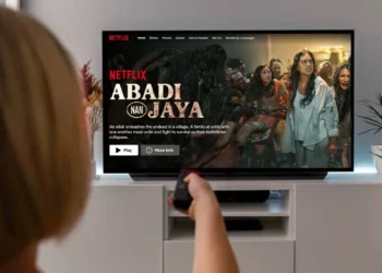 Ilustrasi cara nonton film Abadi Nan Jaya yang sedang trending di Netflix, menampilkan layar TV dengan halaman judul film dan seseorang yang memegang remote.