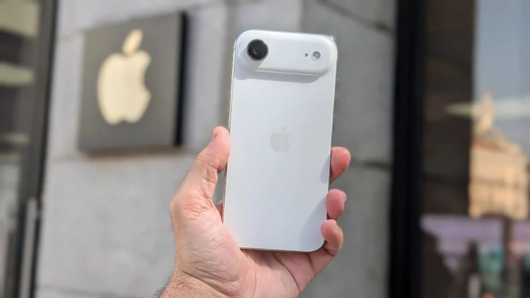 Sebuah tangan memegang konsep iPhone Air berwarna putih di depan logo Apple, menggambarkan spekulasi penurunan produksi iPhone Air.