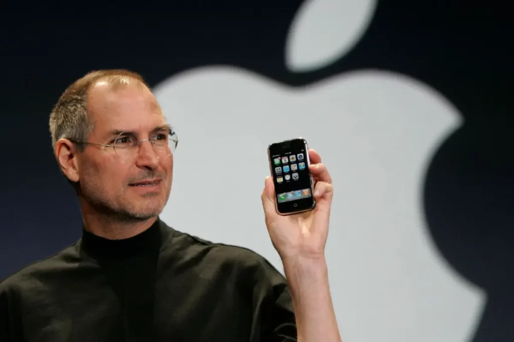 Foto ikonik Steve Jobs saat memperkenalkan iPhone pertama pada tahun 2007, sebuah perangkat yang ditenagai oleh prosesor ARM dan mengubah dunia teknologi.