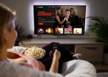 Seorang wanita sedang bersantai sambil memilih tontonan di situs nonton film legal dari smart TV-nya.